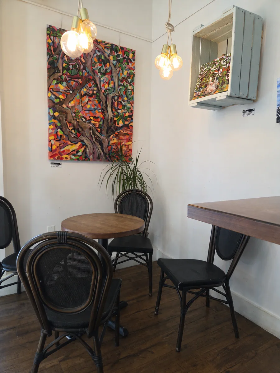 Round café table and dark chairs beside colourful artwork