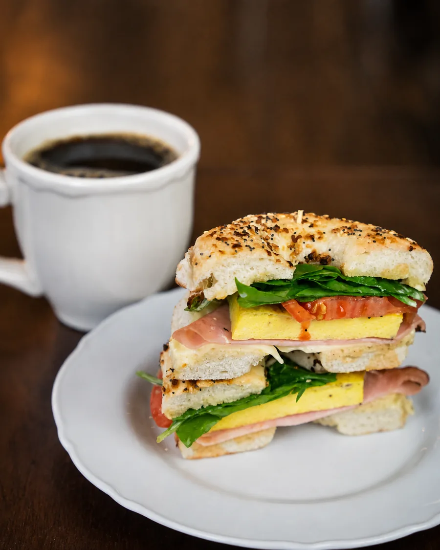 A breakfast bagel sandwich with a cup of coffee